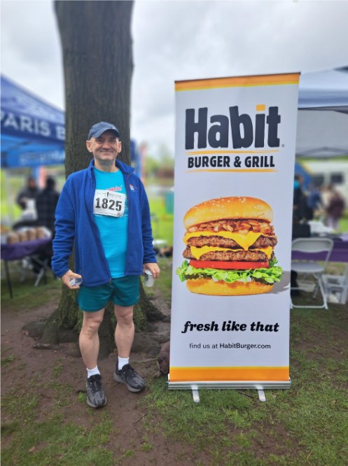 Race participant standing next to a tall Habit Burger & Grill banner at an event